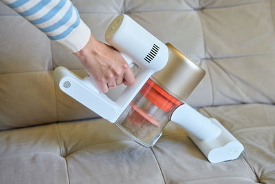 Woman cleaning sofa with vacuum cleaner in living room