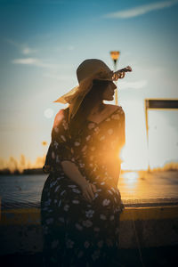 Rear view of woman standing by sea against sky during sunset