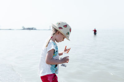 Girl holding umbrella by sea against sky