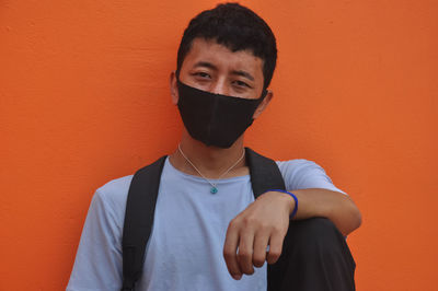 Portrait of young man wearing mask against orange background