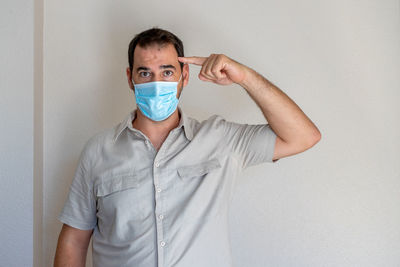 Portrait of man wearing flu mask gesturing while standing against white wall