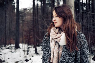 Young woman looking away in forest during winter