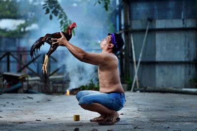 Full length of shirtless man holding rooster