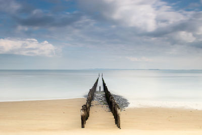 Wooden posts on beach against sky