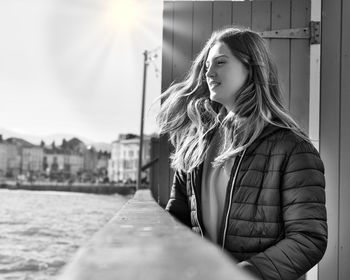 Smiling woman looking at sea while standing by retaining wall in city