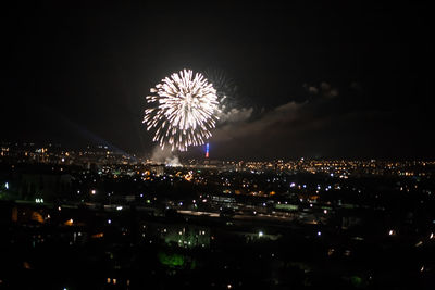 Firework display over illuminated city against sky at night