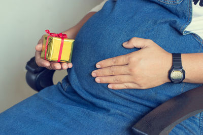 Midsection of pregnant woman holding gift box while sitting on chair
