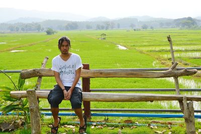 Portrait of man sitting on wooden bench against rice field