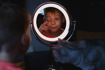 Cat looking at boy reflecting in mirror at home