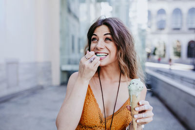 Smiling woman having ice cream while standing against building in city