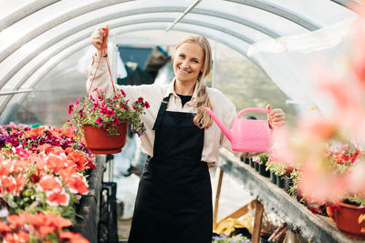 A smiling female gardener works in a greenhouse and enjoys hobbies, tending flowers. 