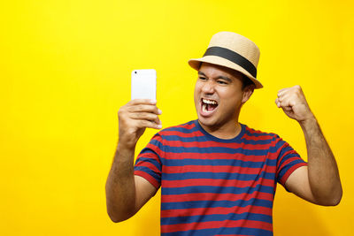 Young woman using mobile phone against yellow background