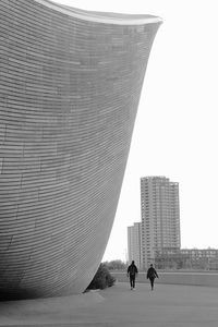 Rear view of men standing by modern buildings in city against sky