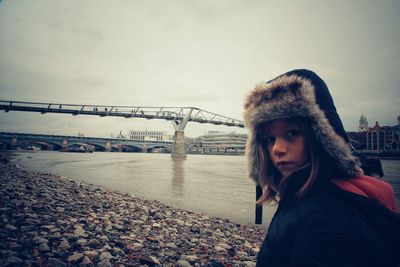 Portrait of girl standing on riverbank against bridge in city