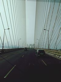 Cars on suspension bridge against sky in city