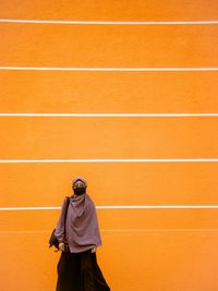 Rear view of man standing against orange wall