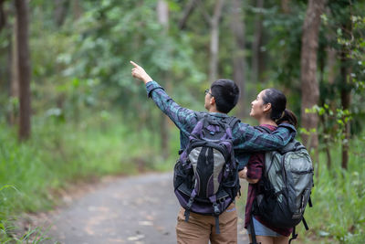 Man showing woman while standing against trees in forest