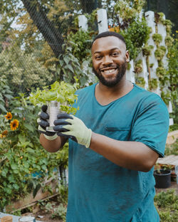 Portrait of smiling male volunteer holding potted plant in community garden