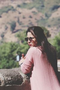 Young woman wearing sunglasses while leaning on retaining wall