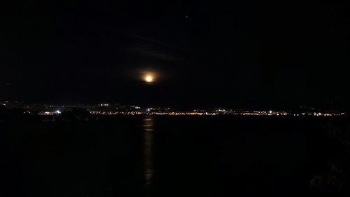 Illuminated city by sea against sky at night