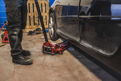 Unrecognizable technician lifting modern vehicle with hydraulic jack during work in professional garage