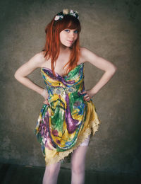 Portrait of woman wearing multi colored dress standing with hand on hip against wall