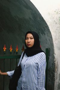 Young woman looking away while standing against wall