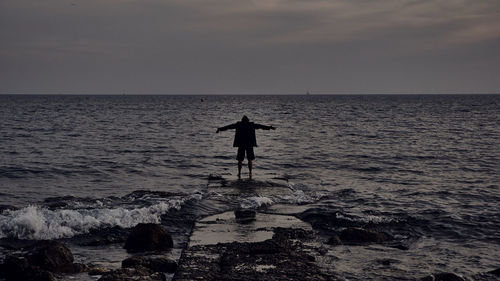 Man standing in sea against sky during sunset