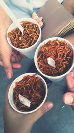 Cropped hands holding food in disposable glasses