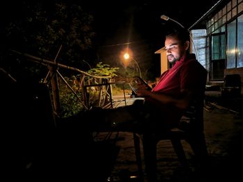 Man using mobile phone while sitting on seat at night