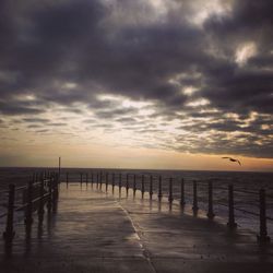 Silhouette pier on sea against dramatic sky