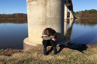 Woman sitting against bridge at lakeshore