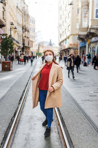 Full length of woman wearing mask standing on tramway in city