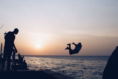 Silhouette person jumping in sea against clear sky