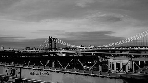 Suspension bridge over river against cloudy sky