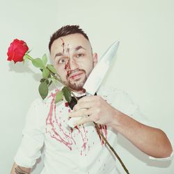 Portrait of young man holding rose against white background