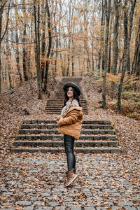 Beautiful young woman standing on stone stairs in forest, autumn, fall, style.