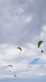 Low angle view of people paragliding against sky