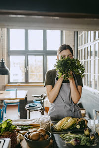 Young female chef smelling fresh cilantro standing in studio kitchen