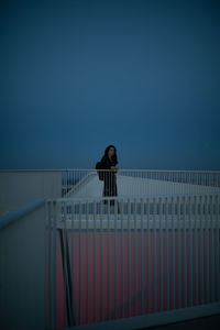 Portrait of woman standing by railing against clear sky