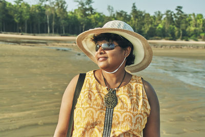 Woman wearing hat and sunglasses standing at beach