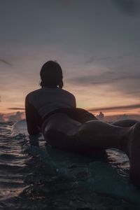 Rear view of woman with surfboard on sea against sky during sunset