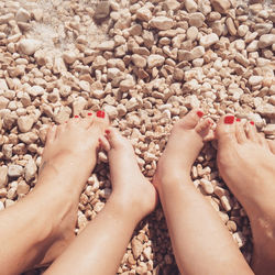 Low section of mother and daughter with red nail polish at beach