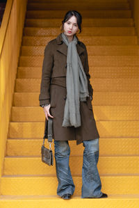 Portrait of young woman standing against yellow wall