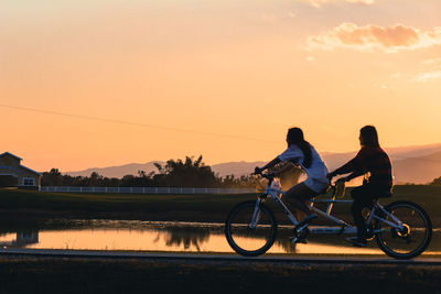 Side view of women on tandem bicycle against sky sunset