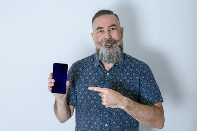 Large bearded caucasian 40-45  showing smartphone screen while pointing at it with the index finger 