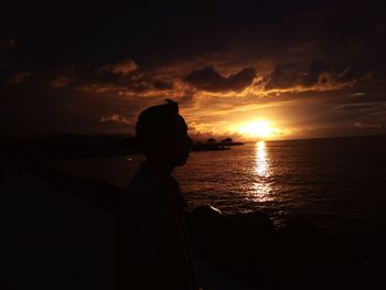 Silhouette man by sea against sky during sunset