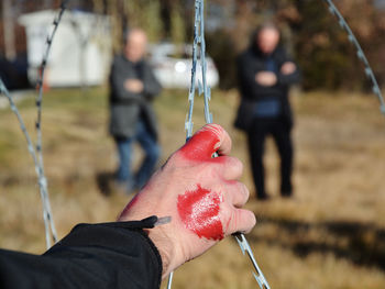 Cropped bloody hand of refugee holding razor wire by standing on field