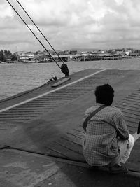 Rear view of people sitting on shore against sky