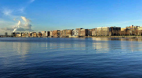Sea by buildings against blue sky